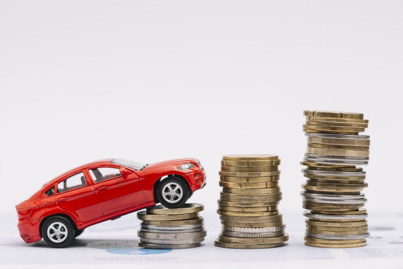 carro-de-brinquedo-subindo-na-pilha-crescente-de-moedas-contra-o-fundo-branco