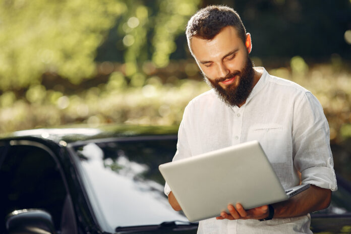 Stylish businessman standing near the car and use the laptop